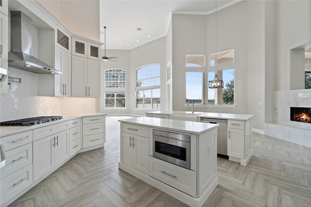 kitchen with white cabinets, a kitchen island, wall chimney range hood, and appliances with stainless steel finishes