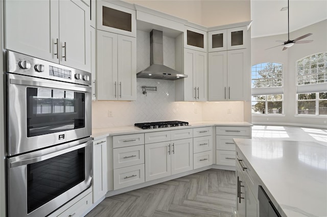 kitchen featuring white cabinets, wall chimney range hood, stainless steel appliances, and ornamental molding