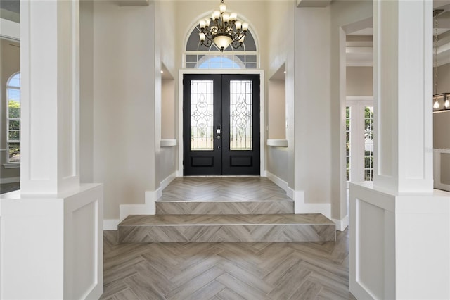 entryway with a towering ceiling, french doors, light parquet floors, and a chandelier