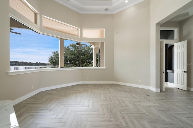 empty room with a wealth of natural light, crown molding, light parquet flooring, and a high ceiling