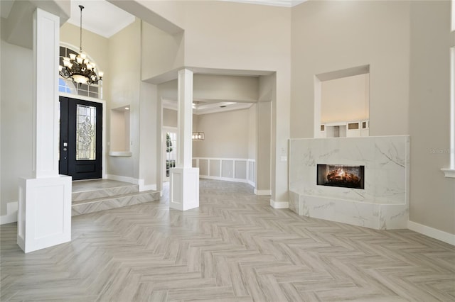 foyer with light parquet floors, a towering ceiling, a notable chandelier, and ornamental molding