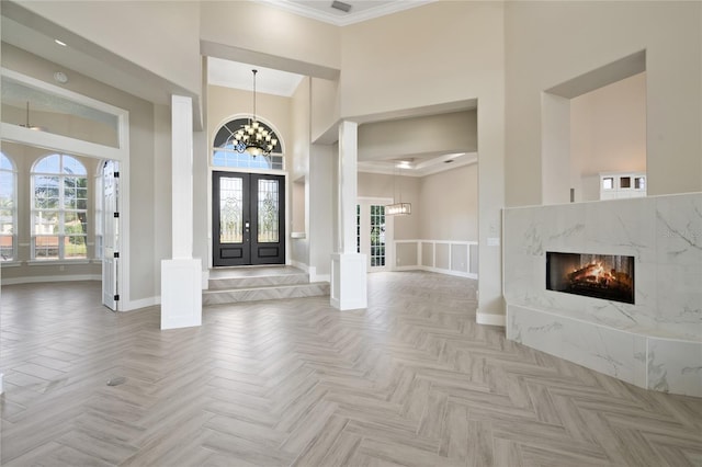 foyer with light parquet floors, ornamental molding, a towering ceiling, and french doors