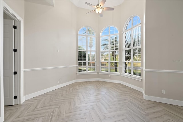 empty room with ceiling fan, a wealth of natural light, and light parquet flooring