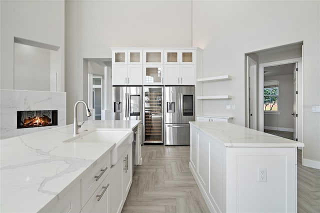 kitchen featuring light stone counters, sink, white cabinets, and stainless steel refrigerator with ice dispenser