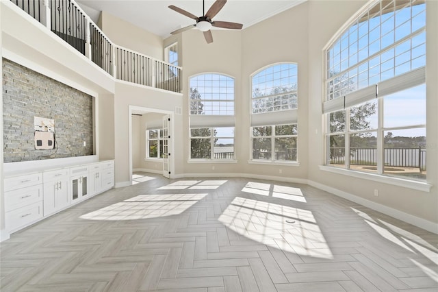 unfurnished living room featuring ceiling fan, a healthy amount of sunlight, a high ceiling, and light parquet floors