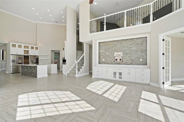 unfurnished living room featuring a towering ceiling, crown molding, and light parquet flooring