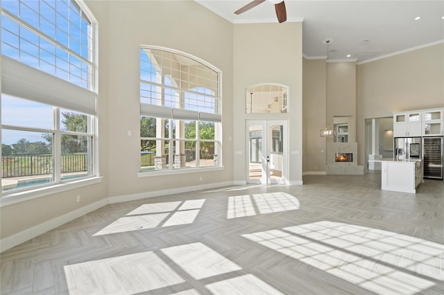 unfurnished living room with plenty of natural light, a towering ceiling, crown molding, and french doors