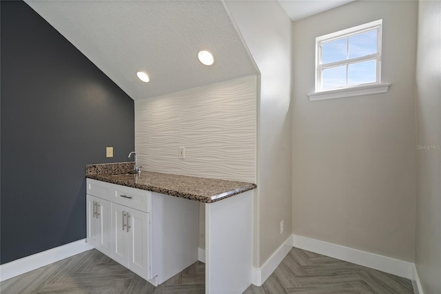 bar featuring dark stone countertops, white cabinetry, lofted ceiling, and parquet flooring