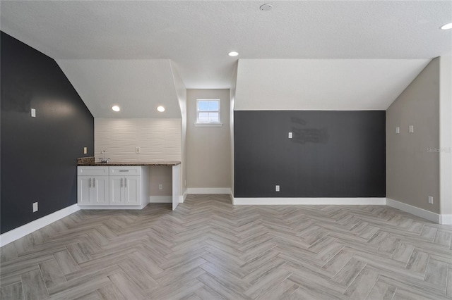 interior space with a textured ceiling, sink, light parquet floors, and lofted ceiling