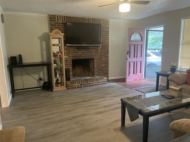 living room with hardwood / wood-style flooring, ceiling fan, ornamental molding, a fireplace, and a textured ceiling