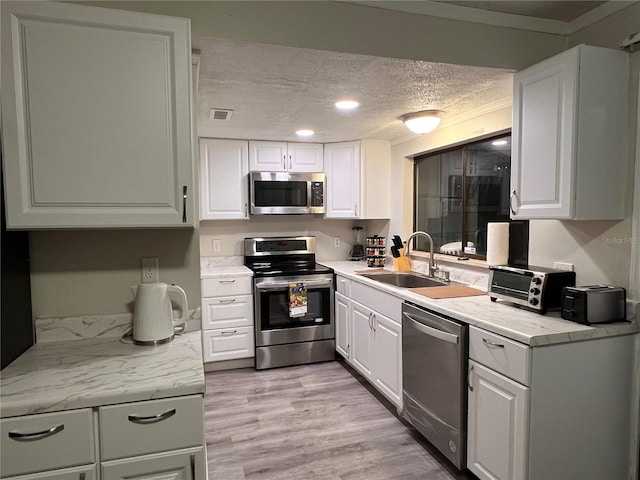 kitchen featuring appliances with stainless steel finishes, a textured ceiling, white cabinetry, and sink