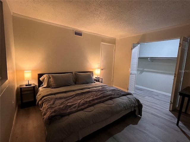 bedroom with a closet, dark wood-type flooring, a textured ceiling, and ornamental molding