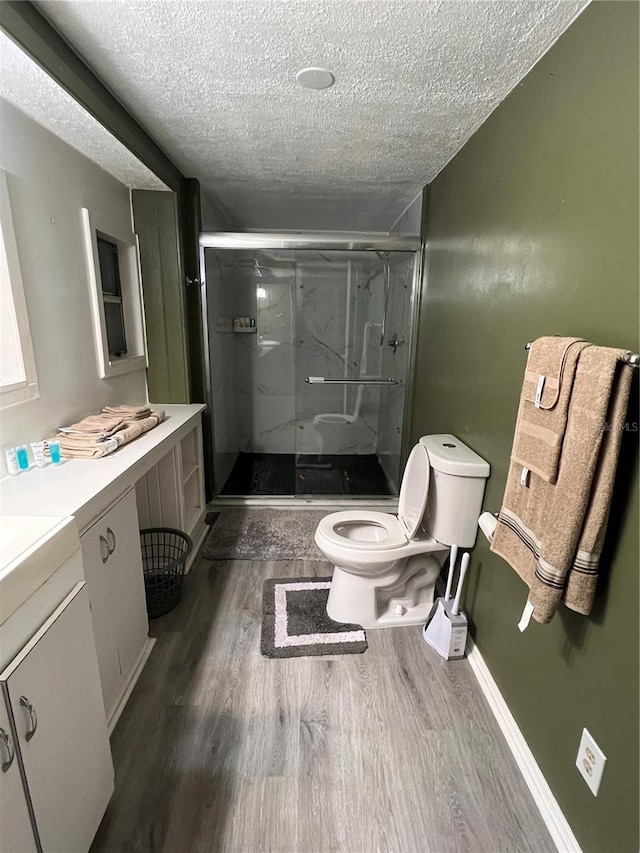 bathroom with a shower with door, wood-type flooring, a textured ceiling, and toilet