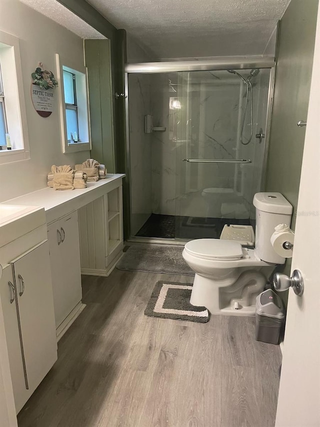 bathroom featuring vanity, a textured ceiling, a shower with door, wood-type flooring, and toilet