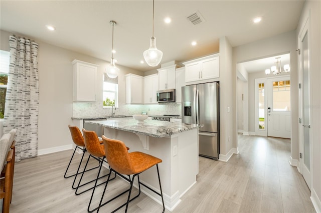 kitchen with white cabinets, light wood-type flooring, appliances with stainless steel finishes, tasteful backsplash, and a kitchen island