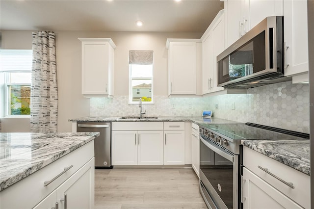 kitchen featuring decorative backsplash, appliances with stainless steel finishes, sink, light hardwood / wood-style flooring, and white cabinetry