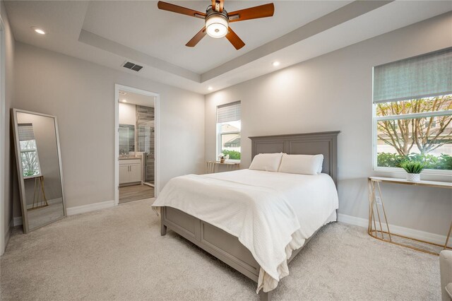 bedroom featuring light carpet, ensuite bath, multiple windows, and ceiling fan