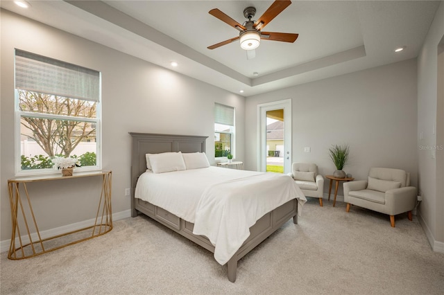 bedroom featuring light colored carpet, a raised ceiling, multiple windows, and ceiling fan