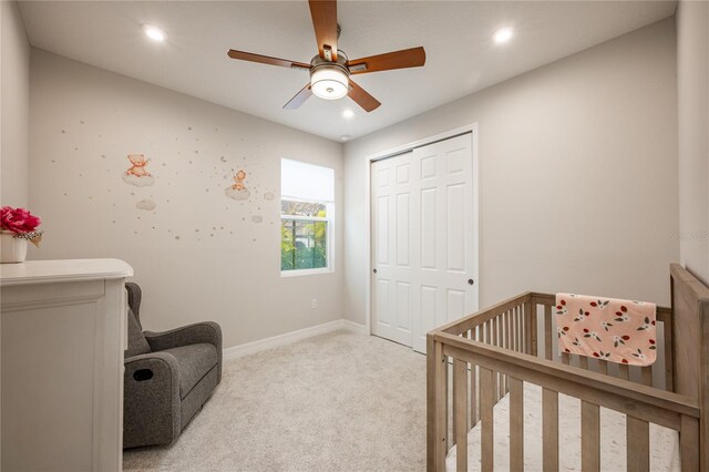 bedroom featuring ceiling fan, a closet, a nursery area, and light carpet