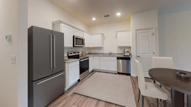 kitchen with white cabinetry, stainless steel appliances, light stone countertops, and sink