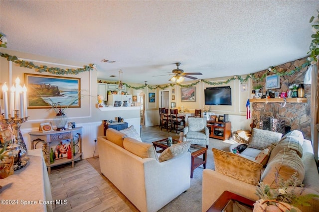 living room with ceiling fan, a fireplace, light hardwood / wood-style floors, and a textured ceiling