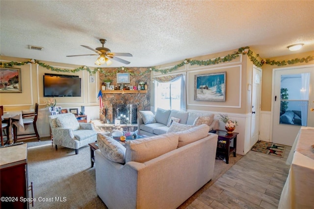 living room featuring a textured ceiling, light wood-type flooring, a stone fireplace, and ceiling fan