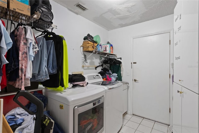 clothes washing area featuring washing machine and clothes dryer, light tile patterned floors, cabinets, and a textured ceiling