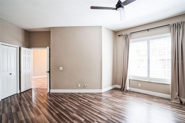 unfurnished bedroom featuring a textured ceiling, baseboards, and dark wood-style flooring