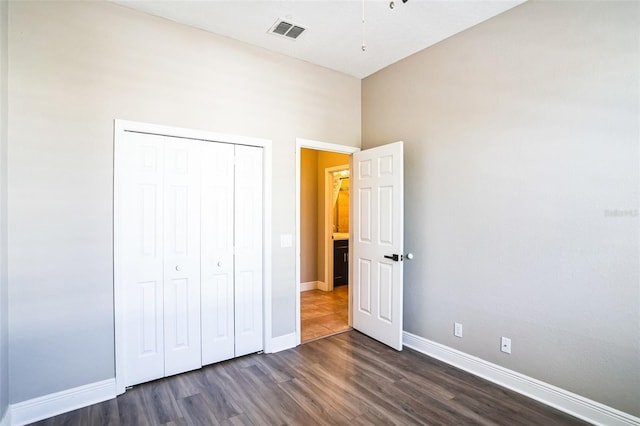 unfurnished bedroom with dark wood-style floors, visible vents, a closet, and baseboards