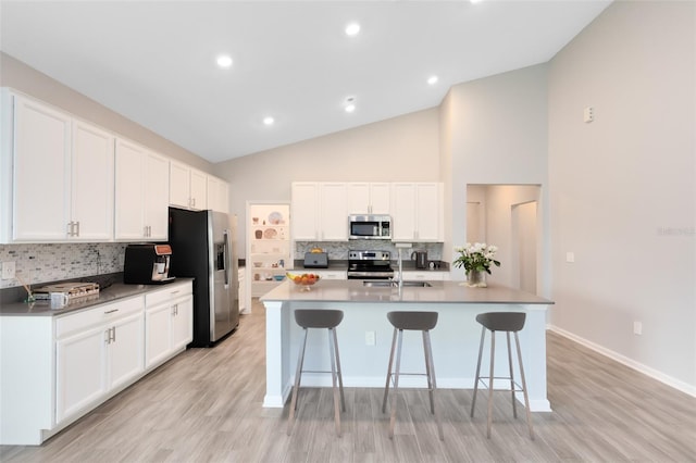 kitchen featuring white cabinets, appliances with stainless steel finishes, a center island with sink, and lofted ceiling