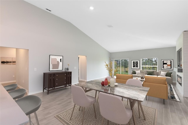 dining room with high vaulted ceiling and light hardwood / wood-style floors