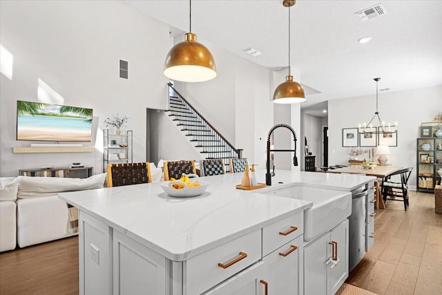 kitchen featuring light wood-type flooring, decorative light fixtures, a kitchen island with sink, and sink