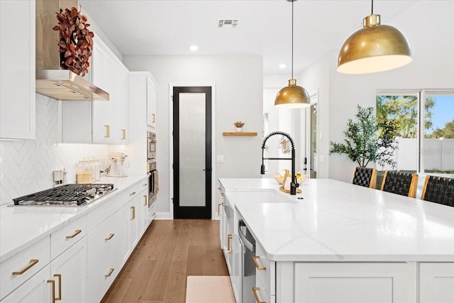 kitchen featuring appliances with stainless steel finishes, decorative light fixtures, a center island with sink, white cabinets, and light wood-type flooring