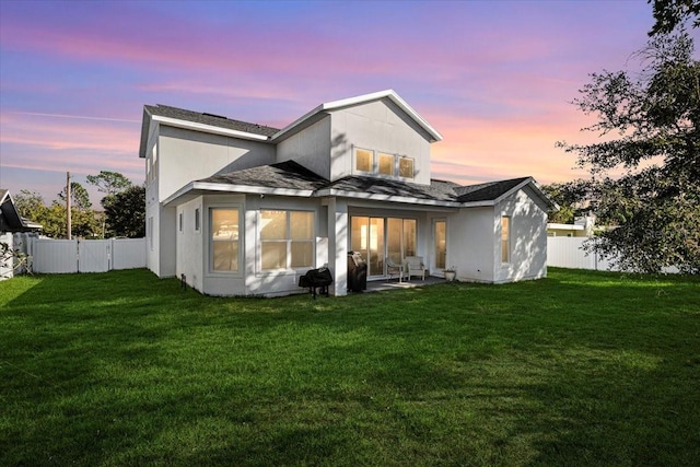 back house at dusk with a yard and a patio