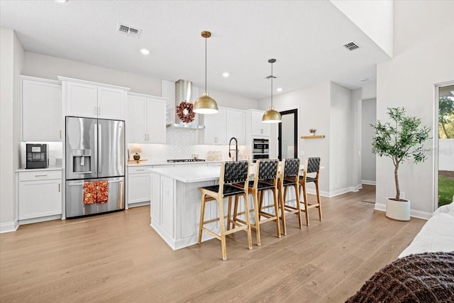 kitchen with stainless steel refrigerator with ice dispenser, light wood-type flooring, wall chimney range hood, a center island with sink, and white cabinets