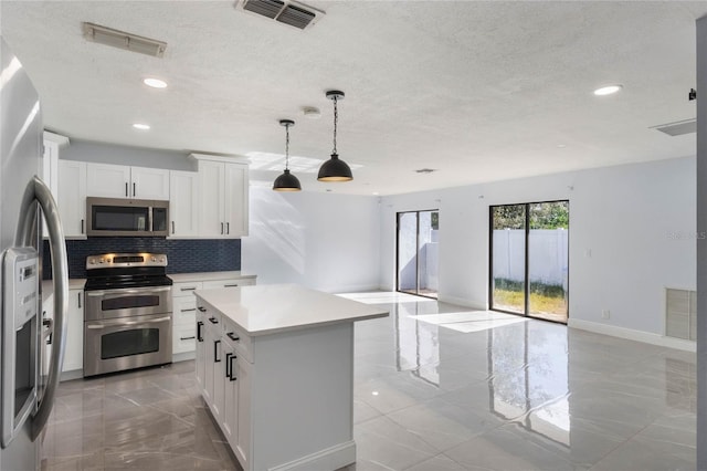 kitchen with decorative backsplash, appliances with stainless steel finishes, white cabinets, a kitchen island, and hanging light fixtures