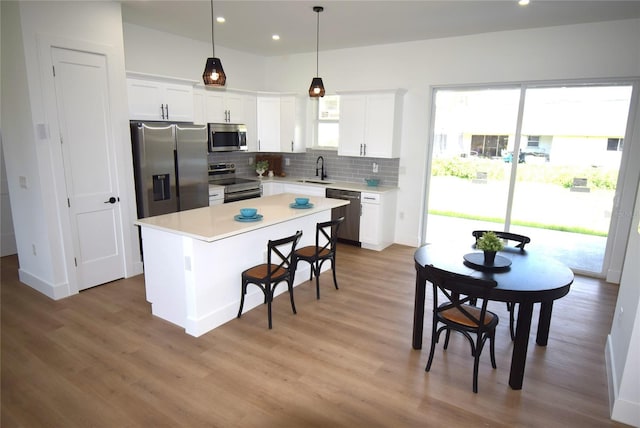 kitchen with white cabinets, stainless steel appliances, decorative light fixtures, and a kitchen island