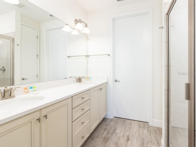 bathroom with double vanity, wood finished floors, a stall shower, and a sink