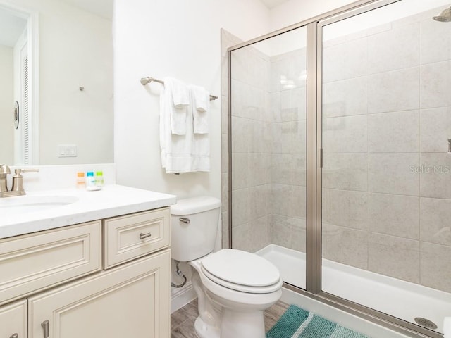 bathroom with toilet, wood finished floors, a shower stall, and vanity