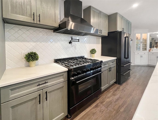 kitchen featuring high quality appliances, backsplash, wall chimney exhaust hood, gray cabinets, and dark hardwood / wood-style flooring