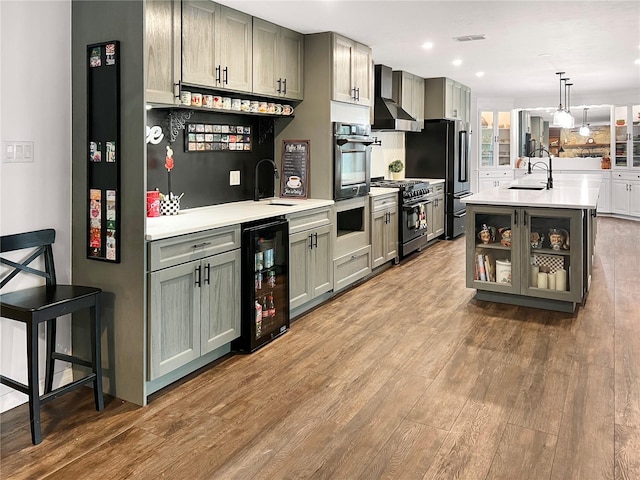 kitchen with hanging light fixtures, wall chimney range hood, wine cooler, gray cabinets, and appliances with stainless steel finishes