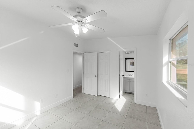 unfurnished bedroom featuring light tile patterned flooring, sink, ceiling fan, ensuite bath, and a closet