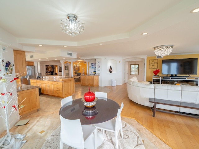 dining area with a tray ceiling, light wood-type flooring, and an inviting chandelier