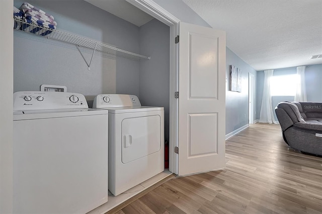 laundry room featuring washer and clothes dryer, light wood-type flooring, and a textured ceiling