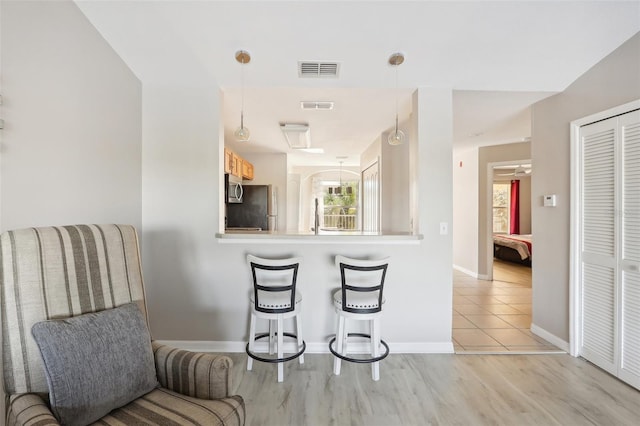 kitchen featuring kitchen peninsula, appliances with stainless steel finishes, decorative light fixtures, and light hardwood / wood-style flooring