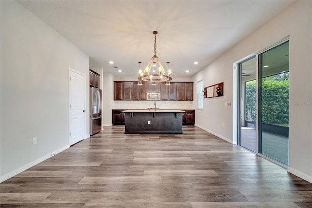 kitchen with hanging light fixtures, an inviting chandelier, stainless steel fridge, hardwood / wood-style floors, and a center island with sink