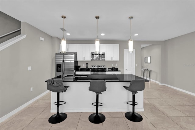 kitchen with a sink, white cabinets, appliances with stainless steel finishes, dark countertops, and a center island with sink