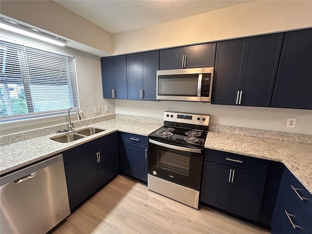 kitchen with sink, light wood-type flooring, blue cabinetry, light stone counters, and stainless steel appliances