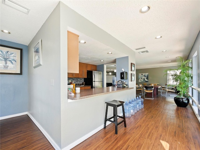 kitchen featuring light wood-type flooring, stainless steel fridge, a textured ceiling, and kitchen peninsula