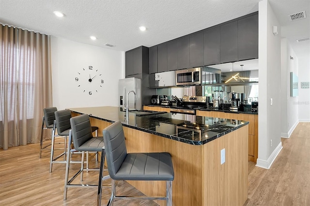 kitchen featuring plenty of natural light, a textured ceiling, a breakfast bar, a center island with sink, and appliances with stainless steel finishes